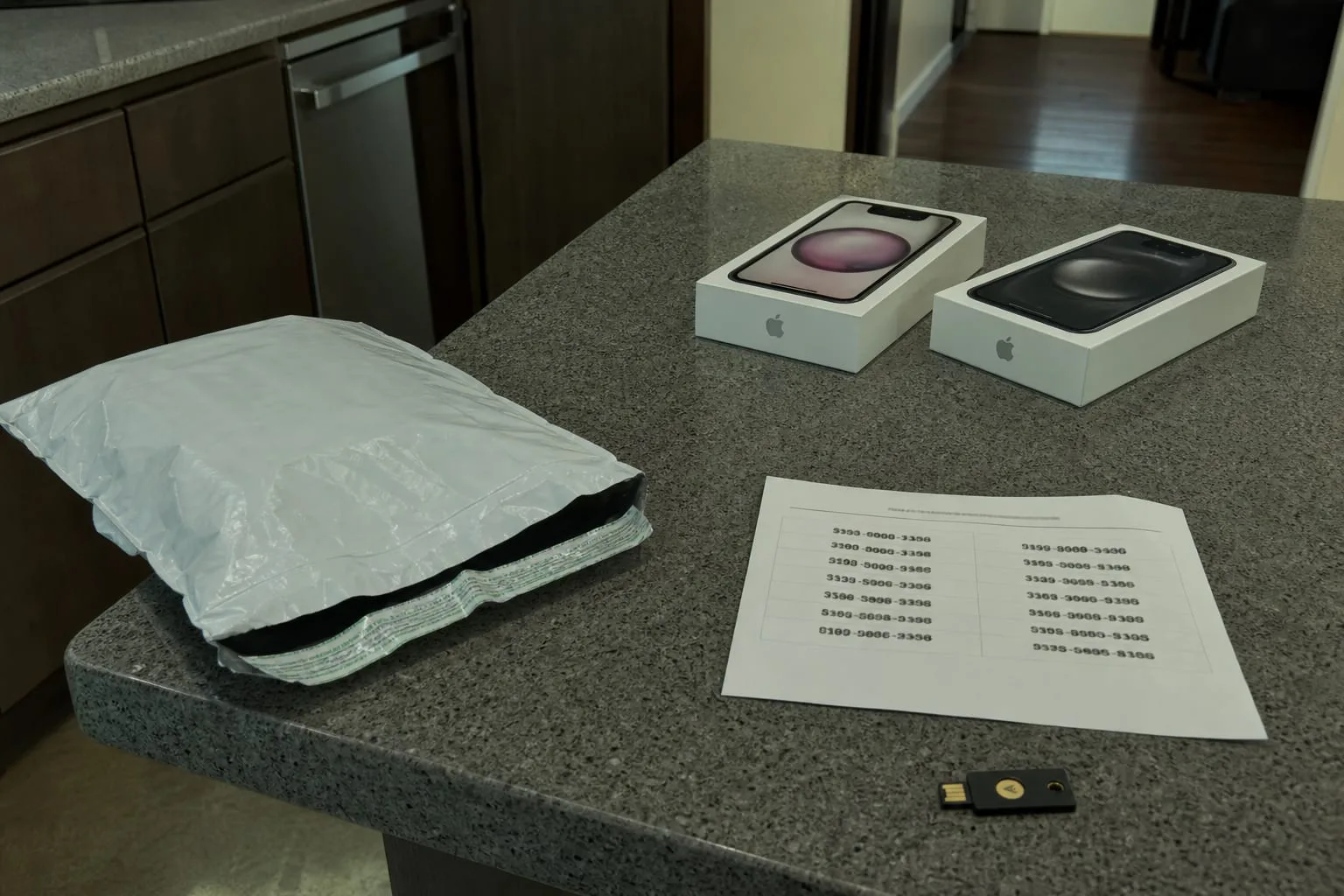 A kitchen counter in early January with two new smartphones still in their boxes, a carrier trade-in mailing envelope, and a printed sheet of one-time recove...